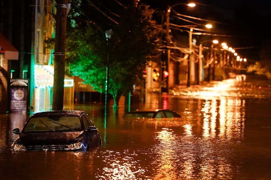 Cars sit submerged under deep floodwaters on a street at night