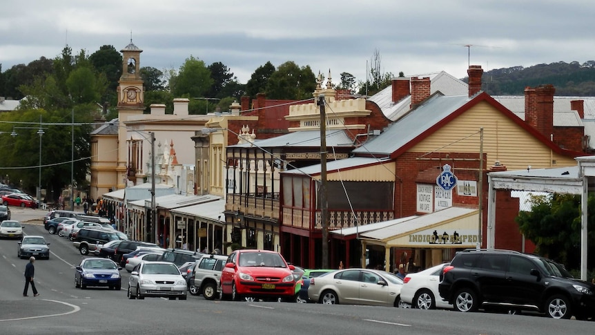 A sloping road in a small town, with cars, shopfronts and a historic clocktower