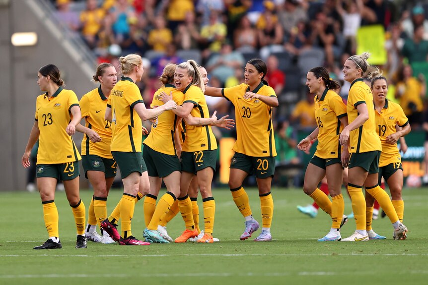 The Matildas players hug and smile wearing gold jerseys