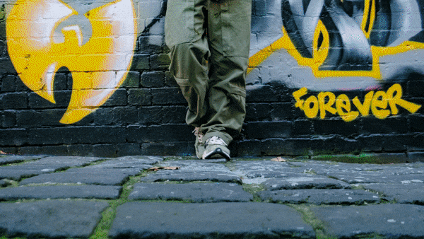 一名穿绿色裤子和球鞋的女士站在涂鸦墙前。