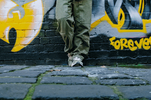 一名穿绿色裤子和球鞋的女士站在涂鸦墙前。