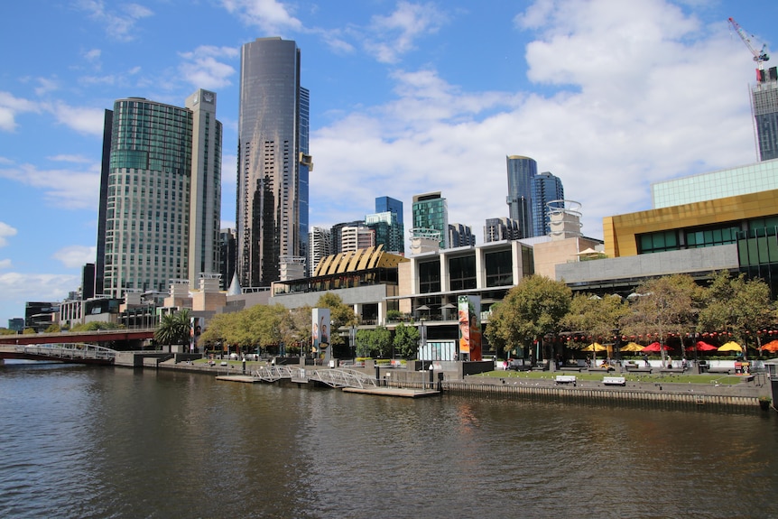 Two highrise buildings and a row of shops, photographed from the other side of a river.