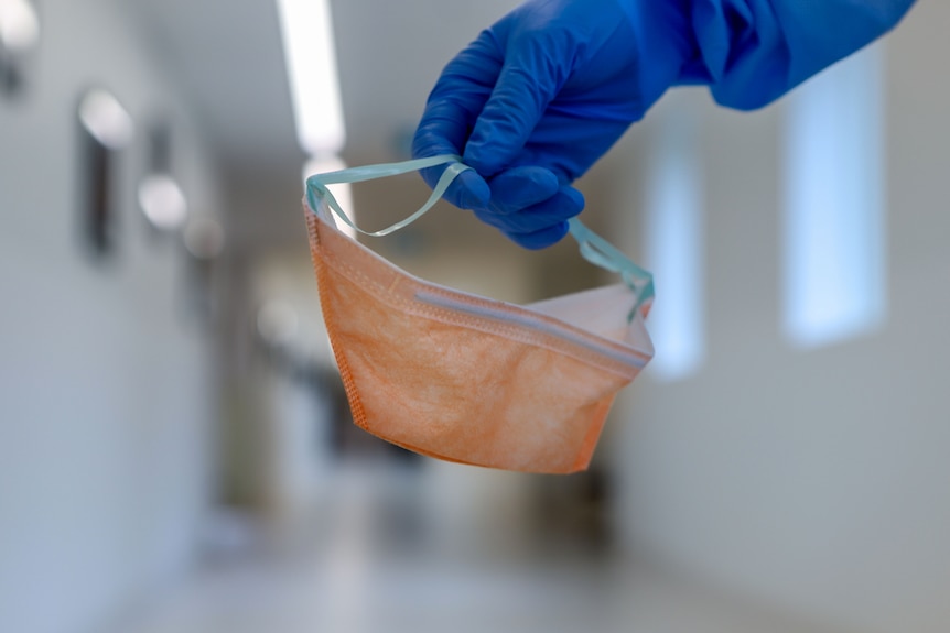 Nurse glove carrying orange PPE mask down hospital corridor