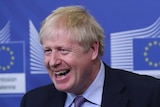 Boris Johnson is smiling while he gives a speech at a podium the European Union logo is in the background