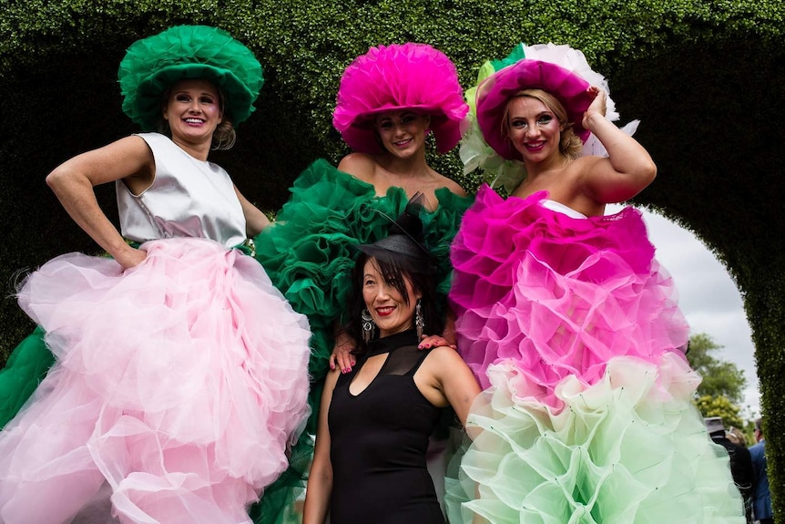 Melbourne Cup racegoers in colourful dresses pose for the camera.