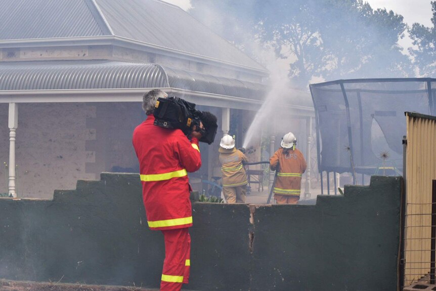 ABC cameraman films as firefighters douse a house in the bushfire path