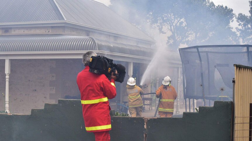 ABC cameraman films as firefighters douse a house in the bushfire path