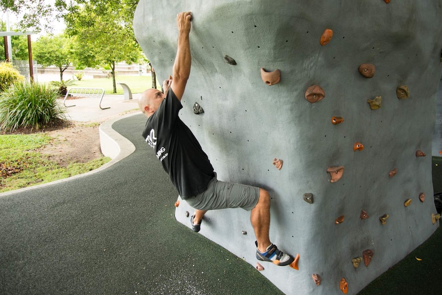 Peter Dumson hangs on to the side of an artificial bouldering wall in Cairns.