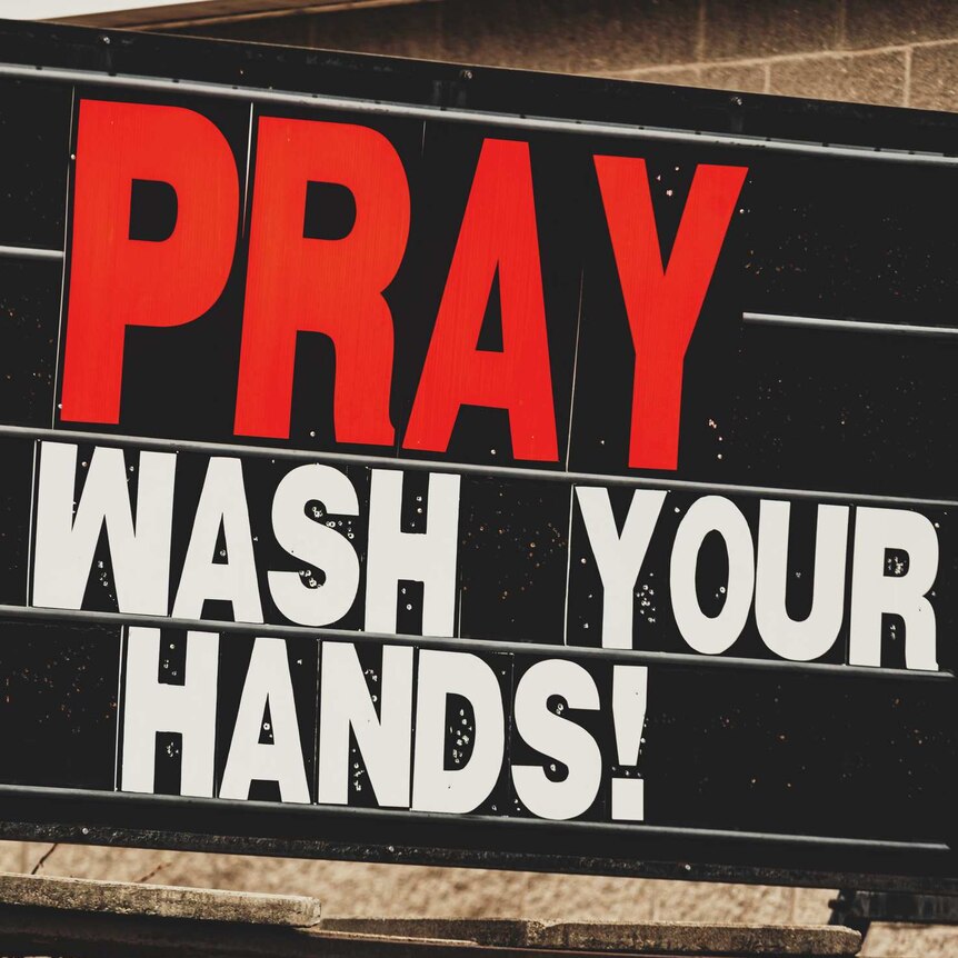 large sign with red and white text 'pray and wash your hands!' in capital letters.