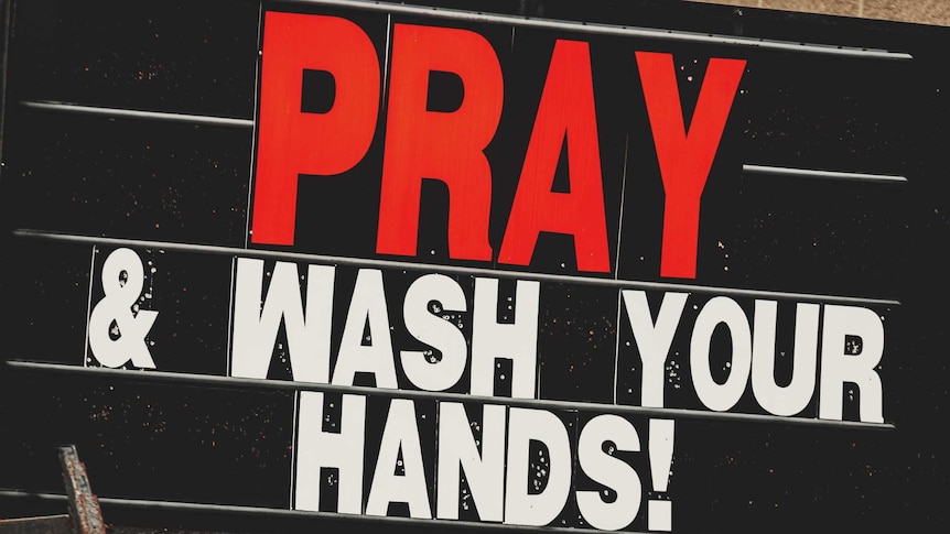 large sign with red and white text 'pray and wash your hands!' in capital letters.