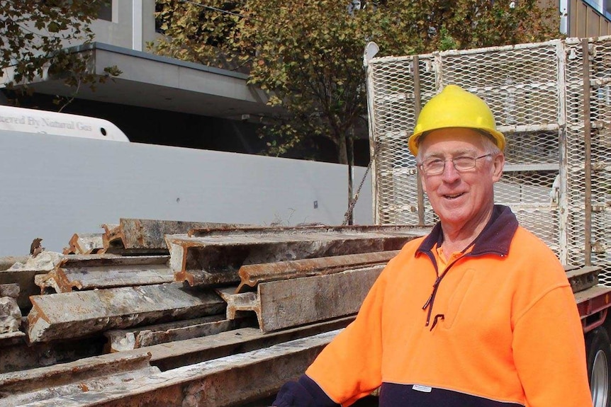 A man wearing hi-vis gear and a hardhat stands in front of a truck carrying old tram tracks.