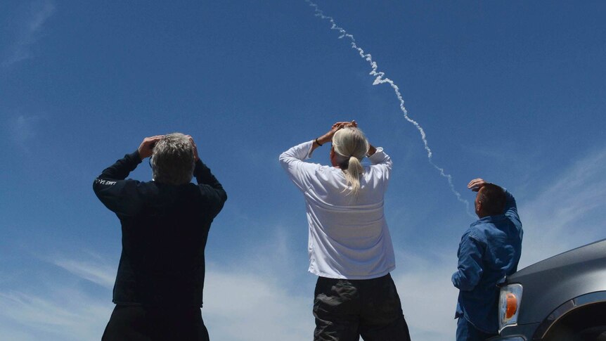 Three spectators watch an interceptor missile traverse a blue sky.
