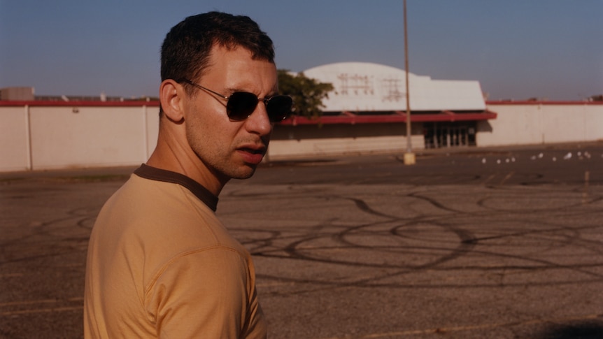 A 2024 press photo of Bleachers frontman Jack Antonoff standing in an empty parking lot with rubber marks