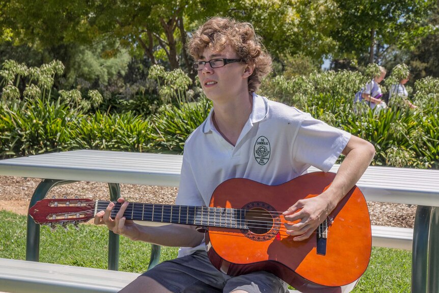 A high school boy sitting on seat playing a guitar