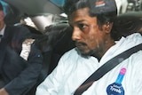 Manodh Marks sits in the back seat of a car wearing a police forensic jumpsuit, as he is driven to court.