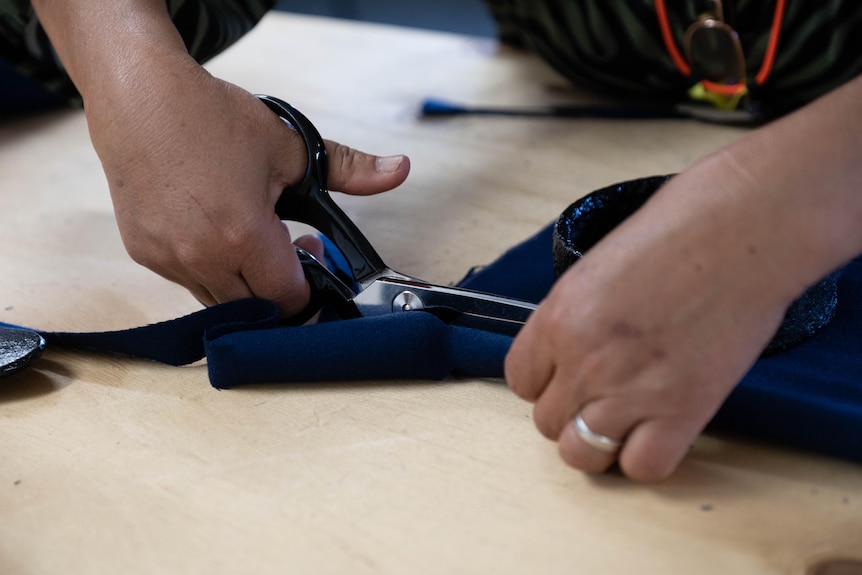 A woman's hands cut fabric on a wooden table. 