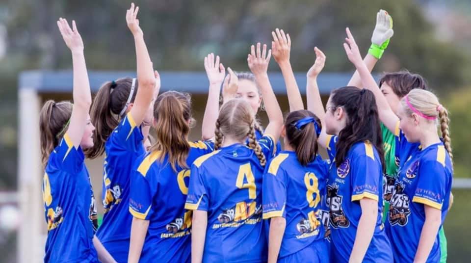 A team of girls in a group with their arms in the air. 