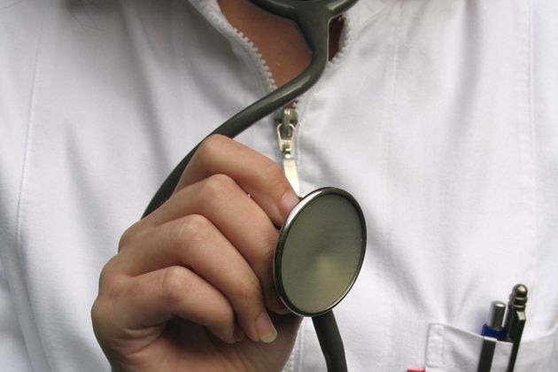 An unidentified female doctor in a white coat holds a stethoscope towards the camera.