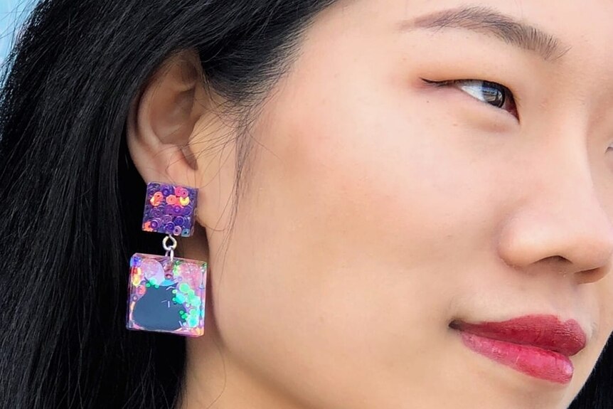 A close up of a model with bright purple and pink earrings.