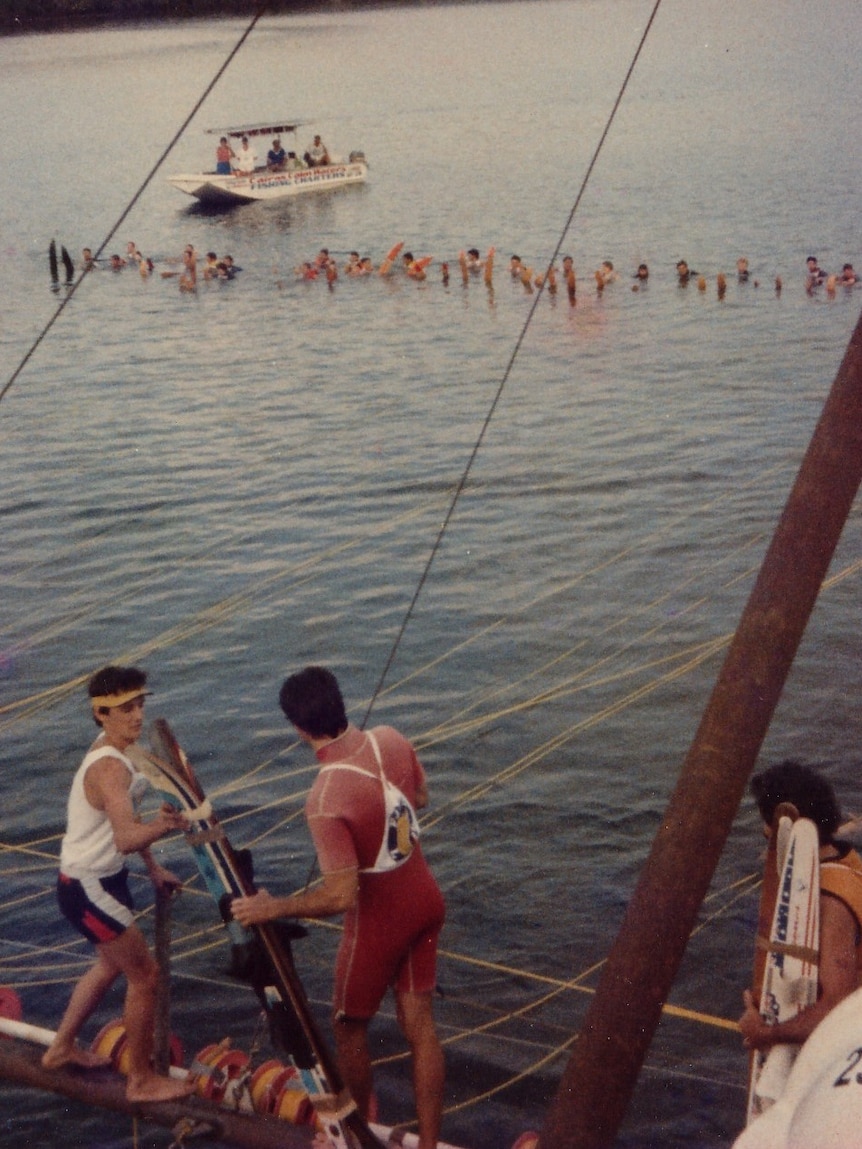 Photo of people with waterskis standing on the boom of a boat with more in the water
