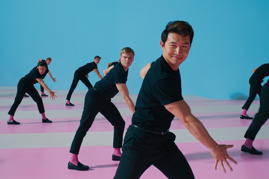 Simu Liu dancing surrounded by other dancing men all in black
