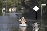 A woman inside a kayak with her dog on a flooded street