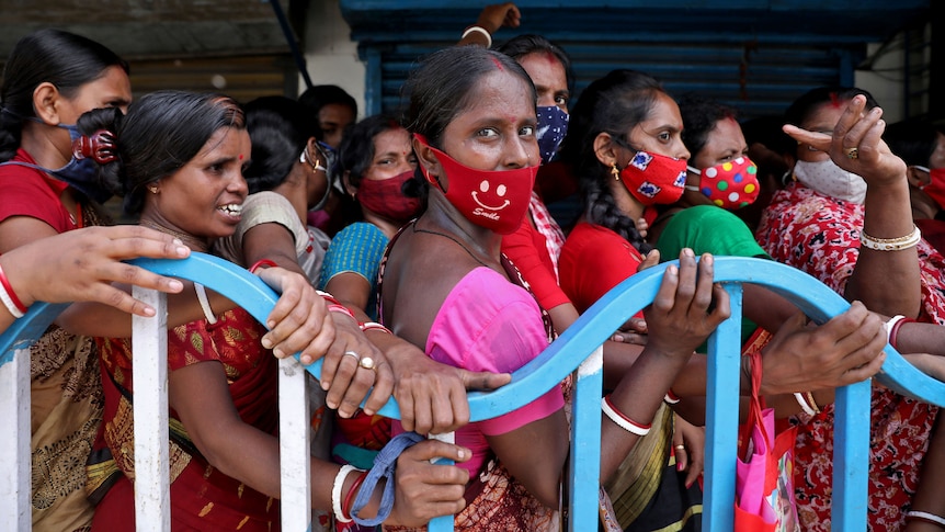 A group of women wait in line behind a fence. 