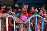 A group of women wait in line behind a fence. 