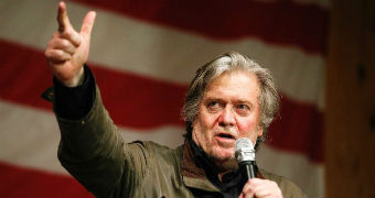 Steve Bannon speaks in a microphone and holds his hand up in the air.