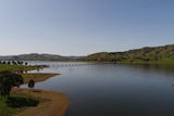 A lake surrounded by green hills and a bridge spans across it