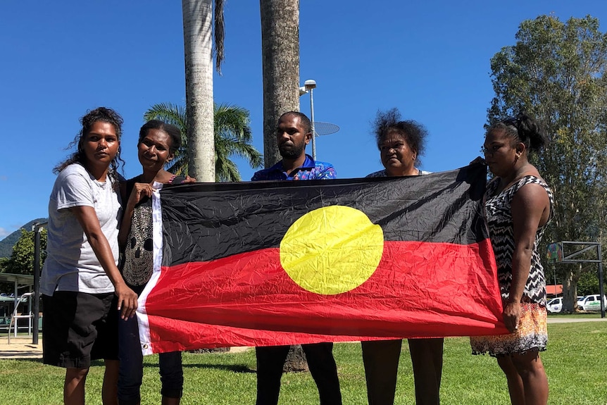 Five people hold up an Aboriginal flag.