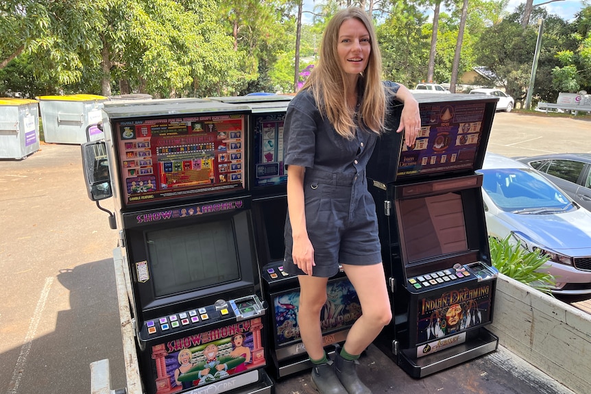 A woman stands on a small truck next to three poker machines