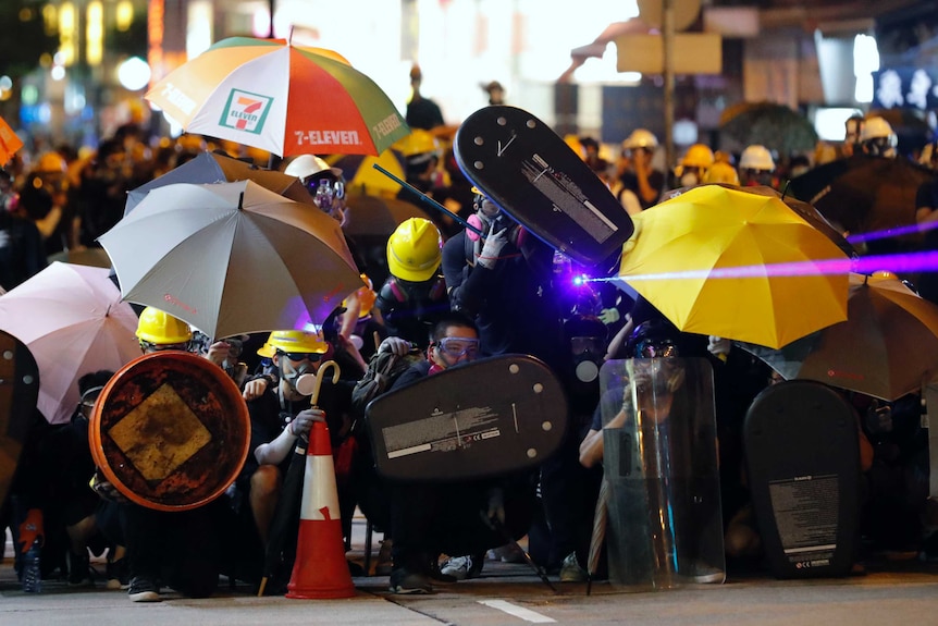 Protesters shine a laser beam as they form up in gas masks and umbrellas during a confrontation with police in Hong Kong