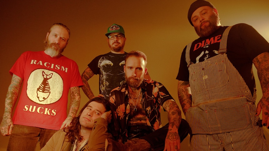Five male members of Alexisonfire look at camera. One wears a shirt saying 'Racism Sucks', one wears overalls, one a trucker cap