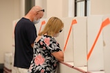 Two people wear face masks cast their votes at polling booths.
