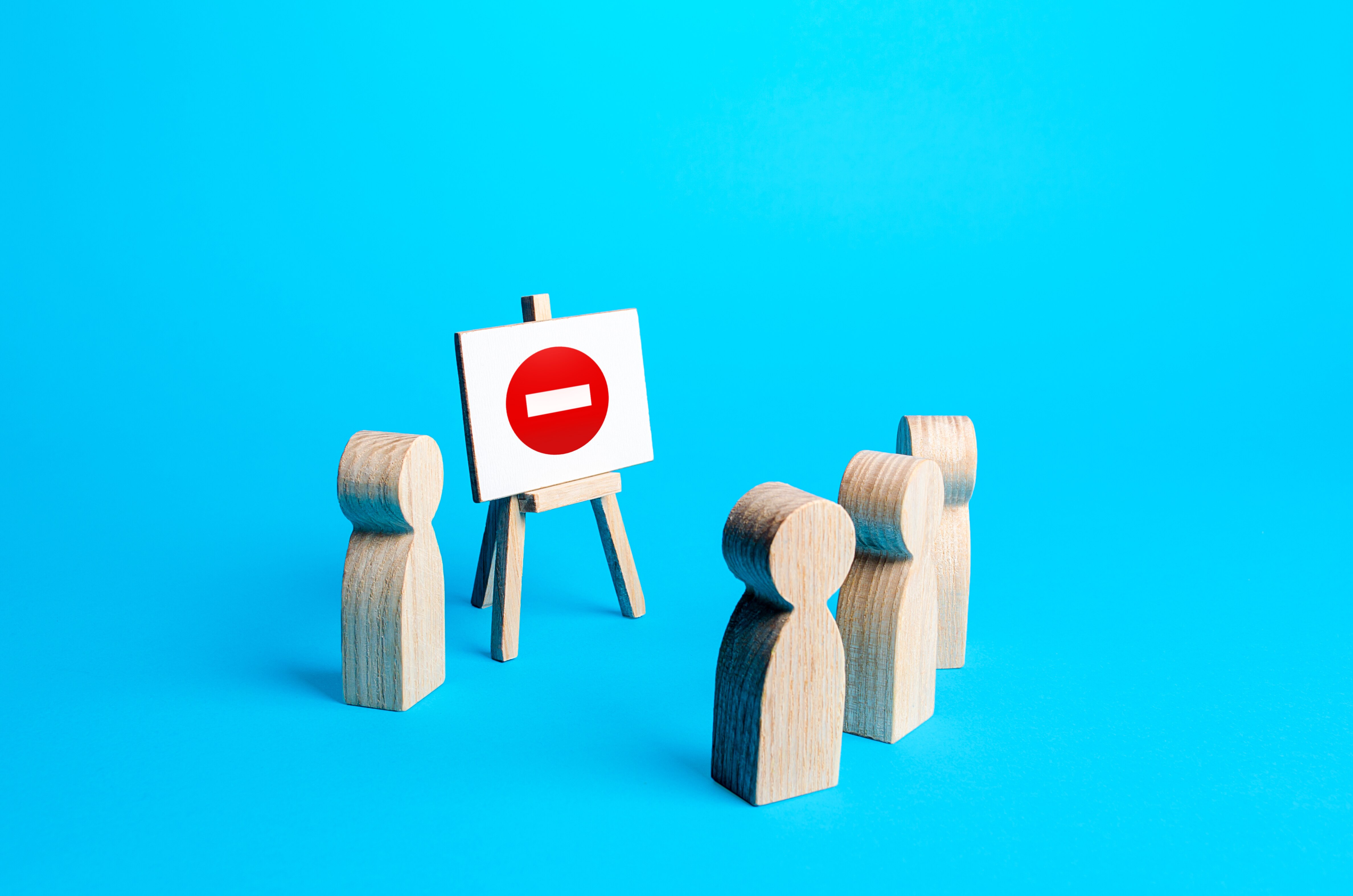 Three wooden blocks shaped like people facing another wooden person giving a presentation.