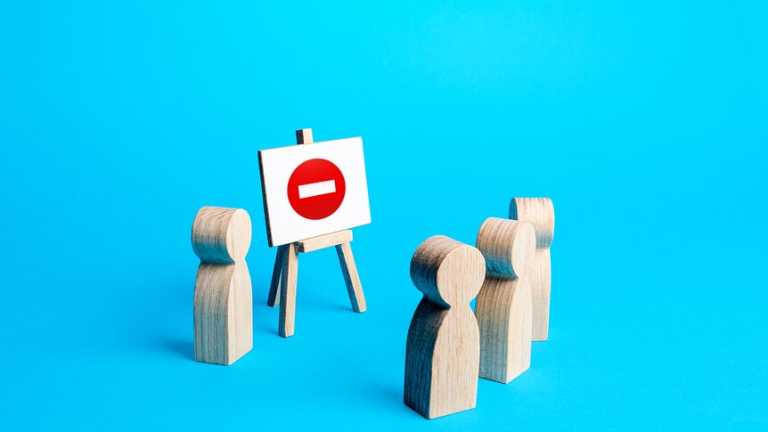 Three wooden blocks shaped like people facing another wooden person giving a presentation.