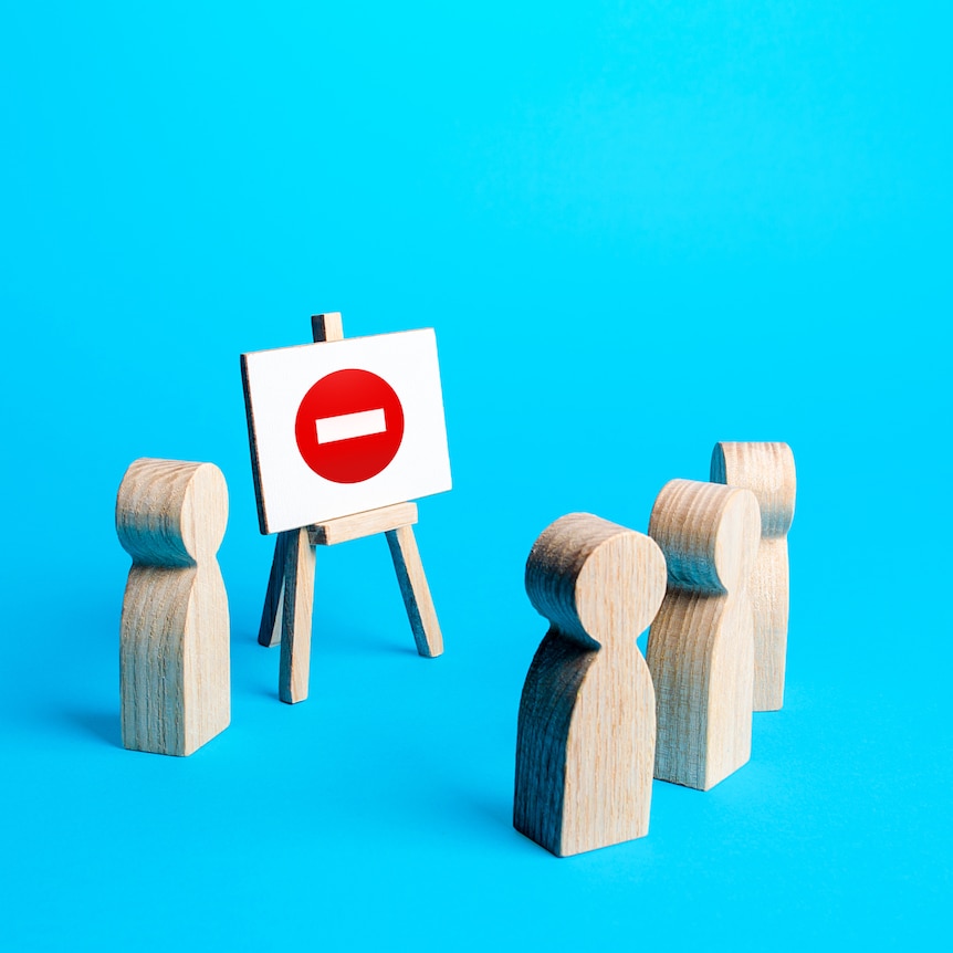 Three wooden blocks shaped like people facing another wooden person giving a presentation.
