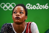 Gabrielle Douglas wears her Team USA uniform in front of a Rio 2016 logo