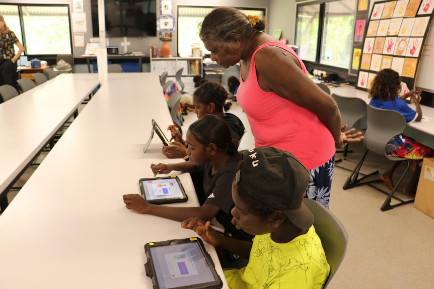 A teacher supervises children using ipads in a classroom.