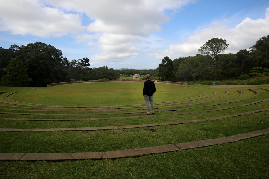 Wide shot of John Bell, pictured from behind, standing in a large outdoor ampitheatre