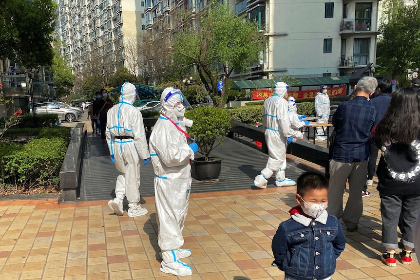 Medical workers in protective suits stand next to a line of residents waiting to take COVID tests