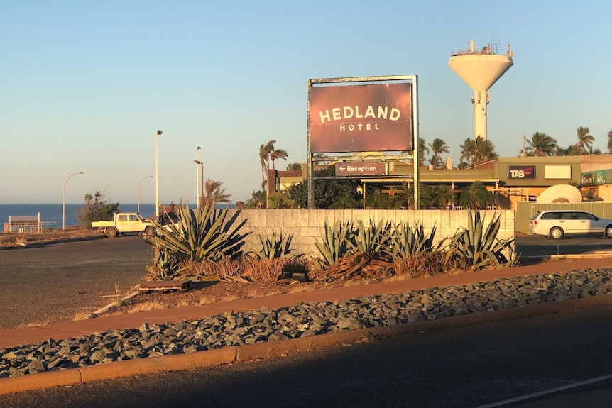 A sign reading 'Hedland hotel' with agave plants in the foreground and a brick hotel building in the background.