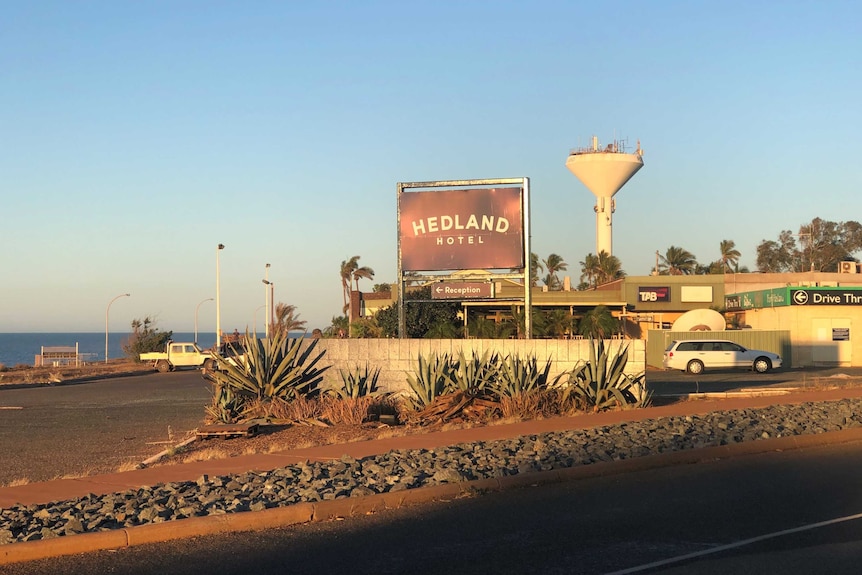 A sign reading 'Hedland hotel' with agave plants in the foreground and a brick hotel building in the background.