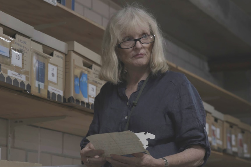 A woman with grey hair and glasses wearing a blue button up shirt and looking through documents.