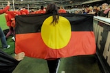 A volunteer holds the Aboriginal flag over the shoulders while walking around the playing arena at the MCG in Melbourne.
