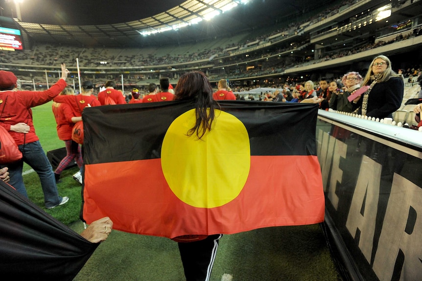 A volunteer holds the Aboriginal flag over the shoulders while walking around the playing arena at the MCG in Melbourne.