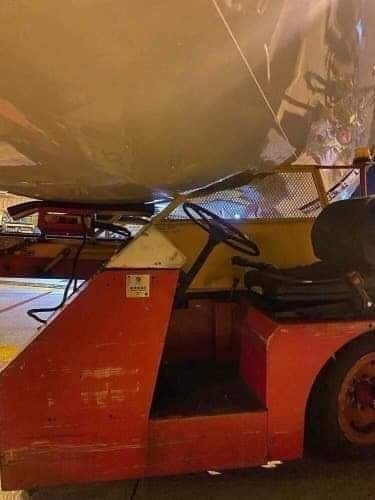 An airport buggy vehicle squashed underneath an airplane after an accident.