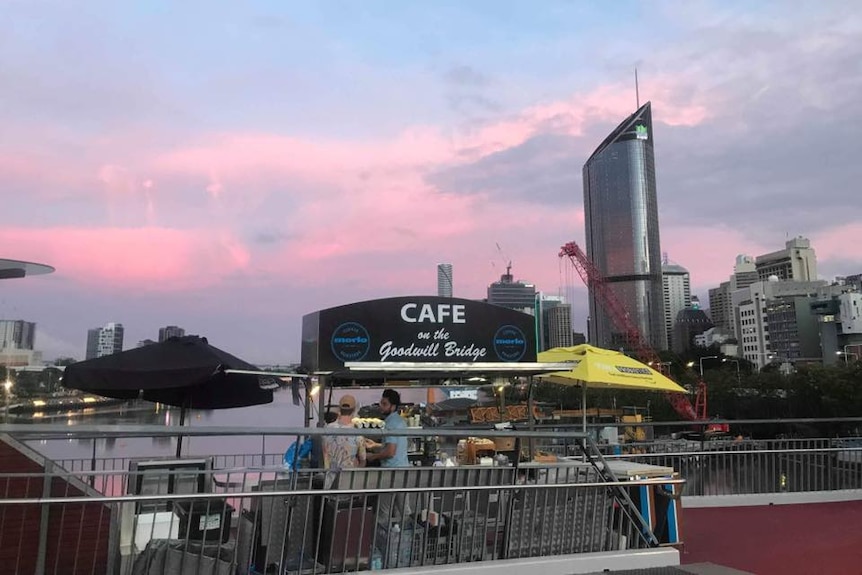 Two people at a coffee stand on a bridge in a city