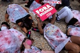Demonstrators are dressed in sheets covered by fake blood lying on the ground.